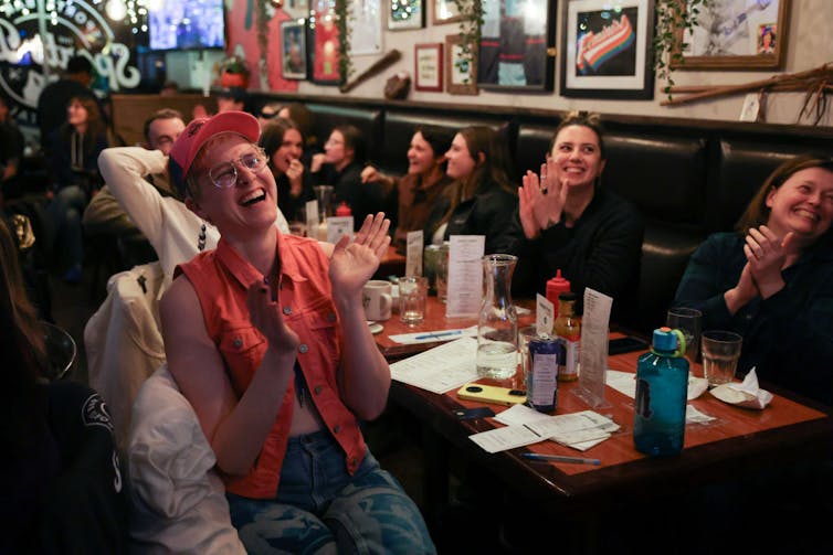 Young women smile and clap while seated at a restaurant table.