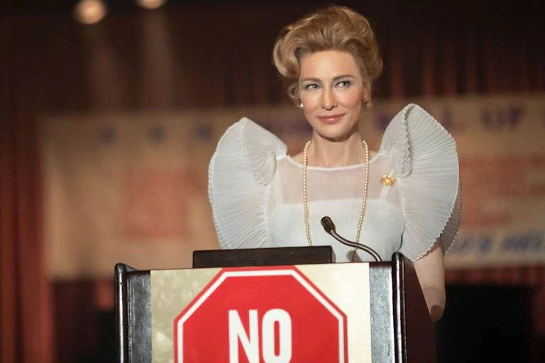 Una mujer guapa, rubia, vestida de forma elegante, habla desde un atril.