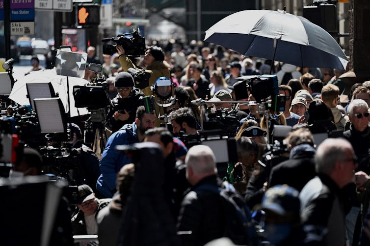 A large crowd of people gather on the streets with fancy and large cameras.