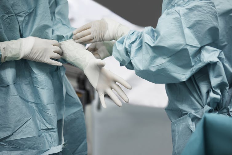Surgeon helps another surgeon put on gloves