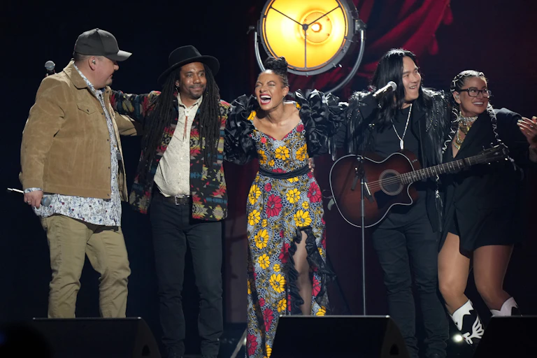 People seen on a stage, one holding a guitar and one holding a microphone.