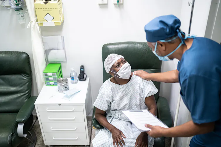 Chirurgien posant la main sur l’épaule d’un patient en blouse et bonnet d’hôpital