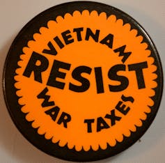 A protest pin reads 'Resist Vietnam War taxes.'