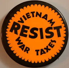 A protest pin reads 'Resist Vietnam War taxes.'