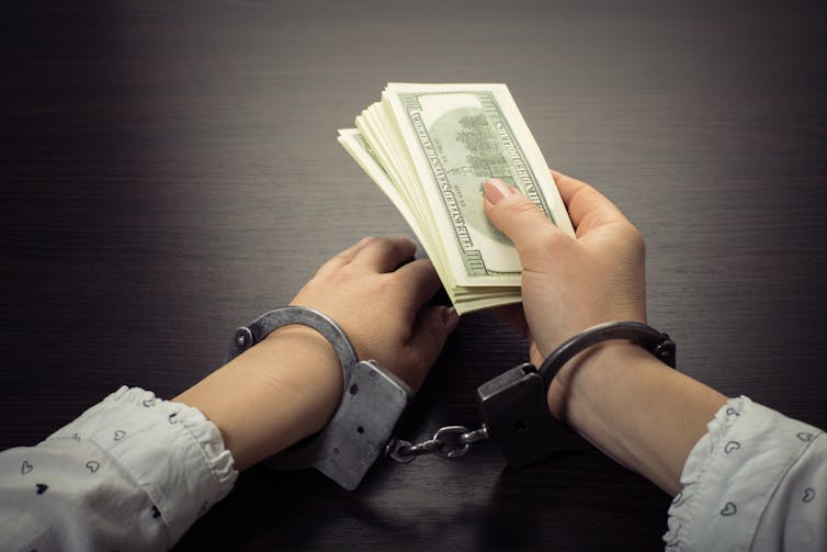 A person holding cash wears handcuffs around his wrists.