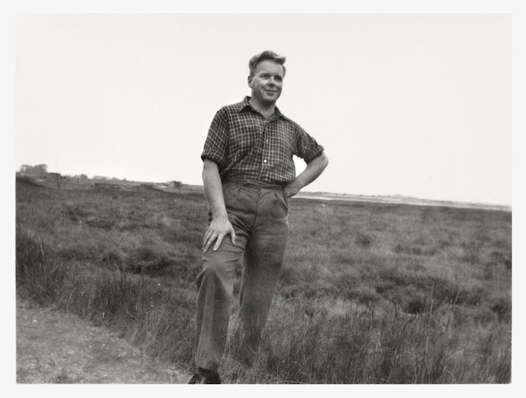 Man in shirt and trousers standing on grassy marshland, sky in background