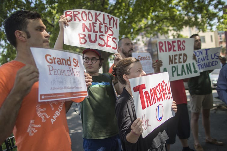 People hold signs reading 'Brooklyn Needs Buses' and 'Riders Need a Plan'