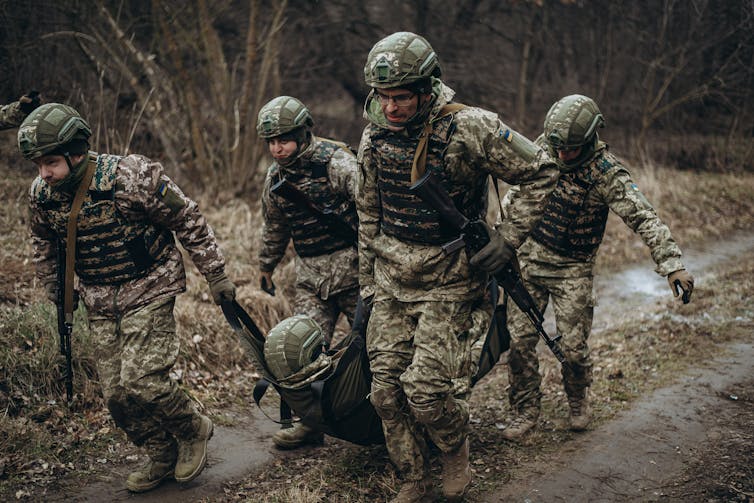 Four people dressed in camp carry a person between them.