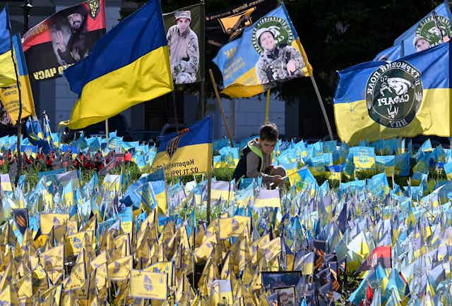 A boy sits among many yellow and blue flags, including some with photos of soldiers and Ukrainian writing.