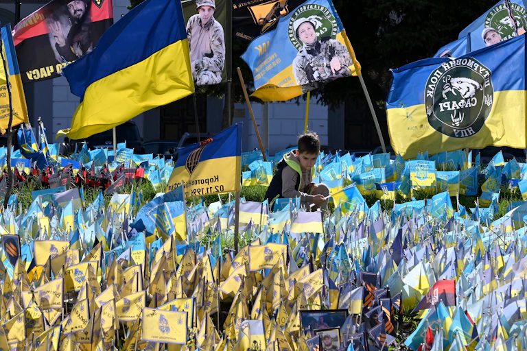A boy sits among many yellow and blue flags, including some with photos of soldiers and Ukrainian writing.
