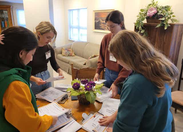 A group of young women sort through piles of paper on a table