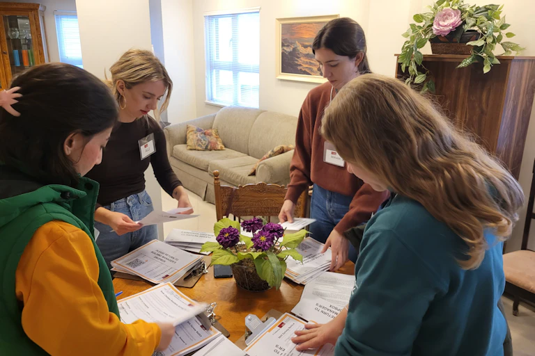 A group of young women sort through piles of paper on a table