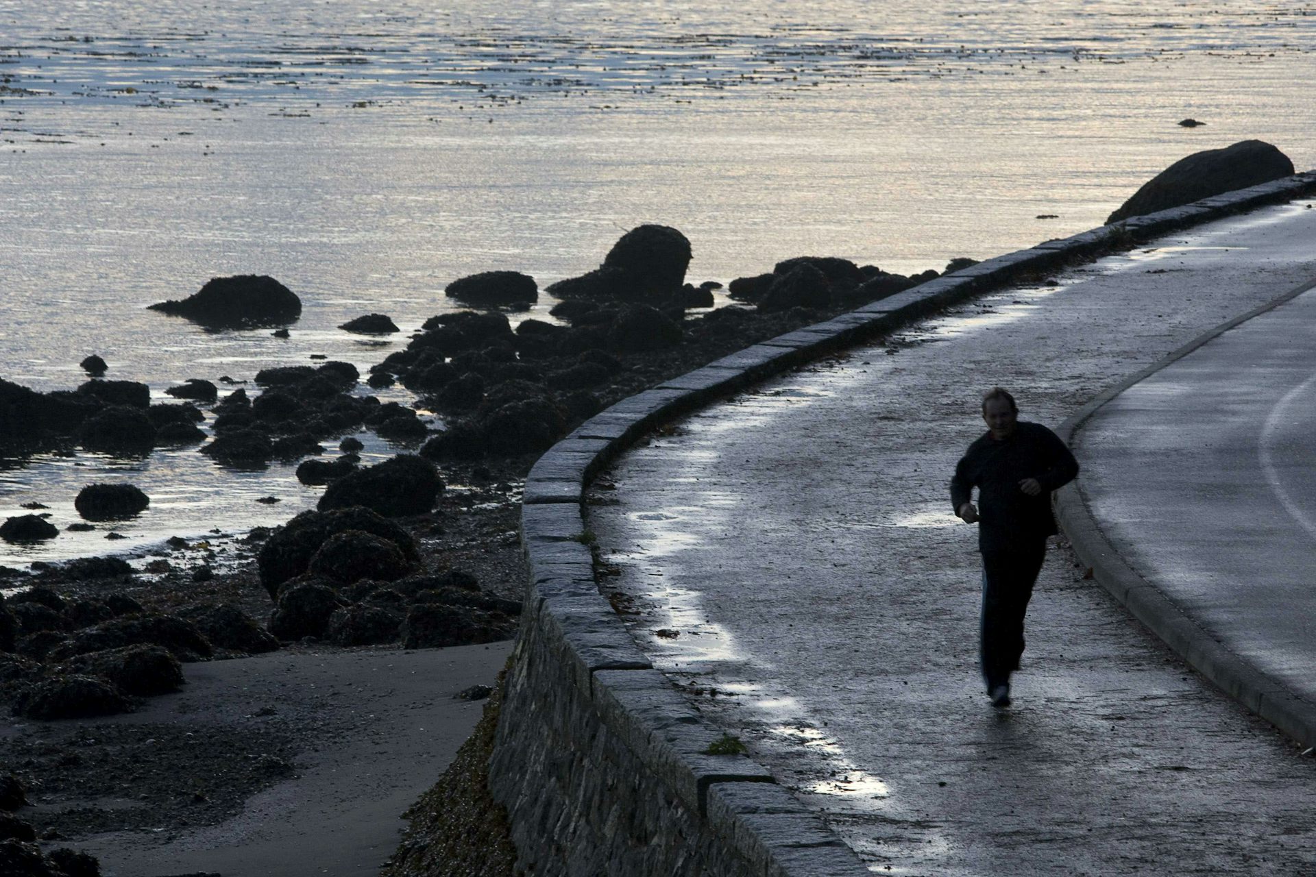 A jogger runs along a seawall next to the sea.