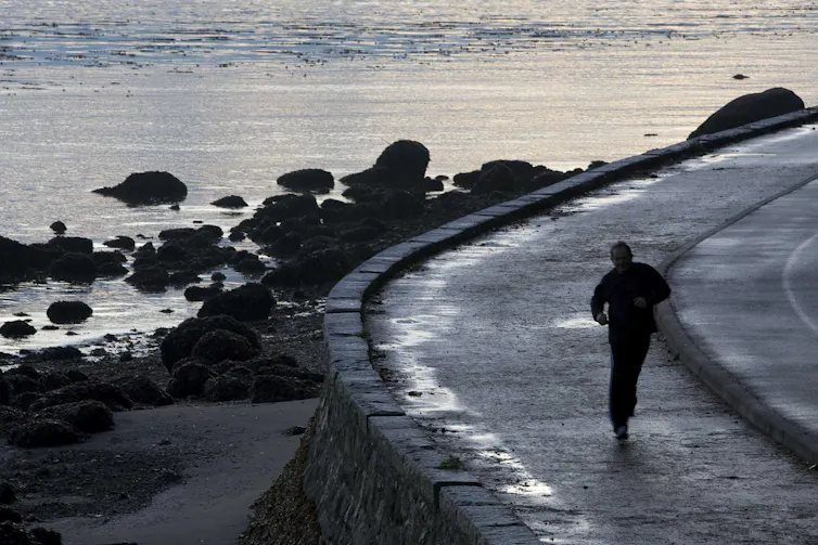 A jogger runs along a seawall next to the sea.