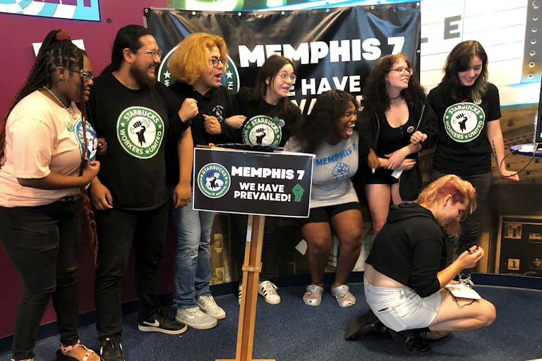 Young people in Starbucks-themed t-shirts lock arms and smile.