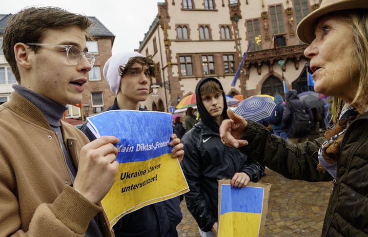 People holding blue and yellow posters stand in the rain.