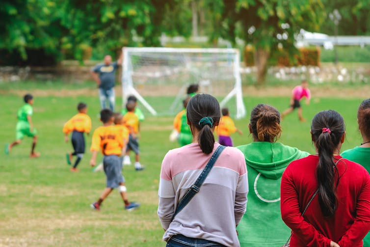 Adults watch young people playing soccer on green oval