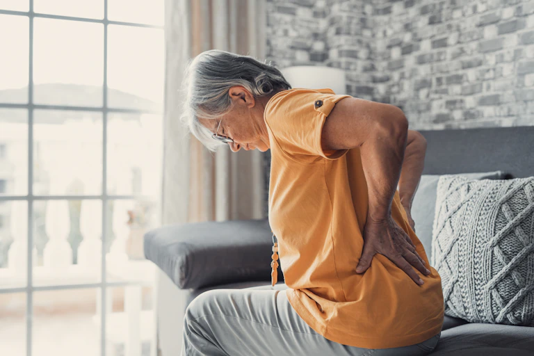 A senior woman holding her lower back in pain.