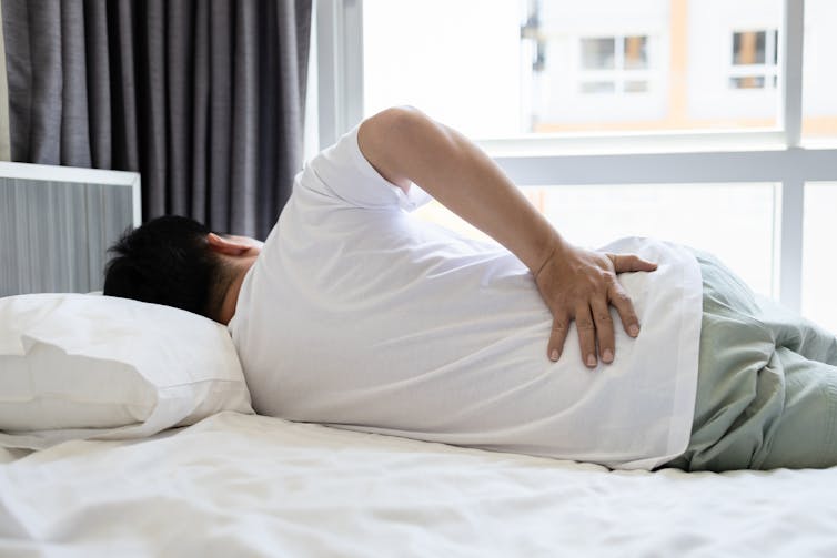 A man lying on a bed with a hand on his lower back.