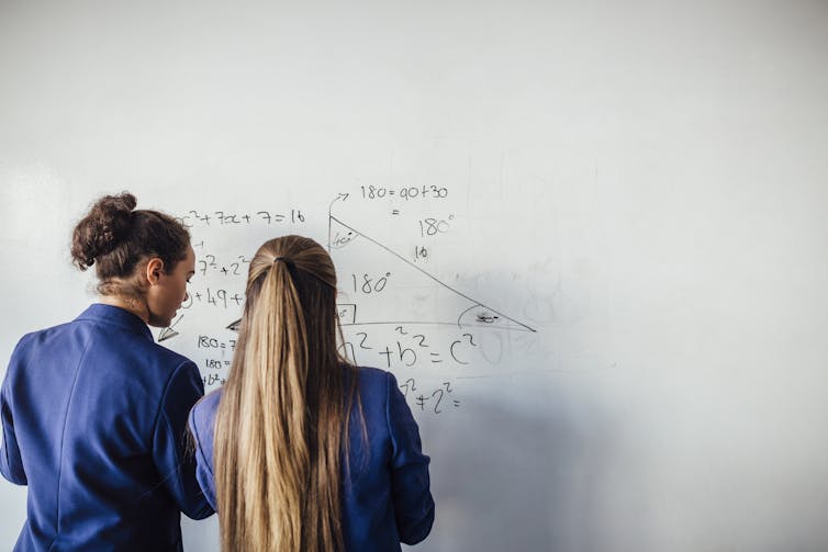Two students work on maths problems at a whiteboard.