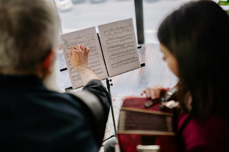 Man Pointing at Notes on a Music Sheet and Girl Playing an Instrument