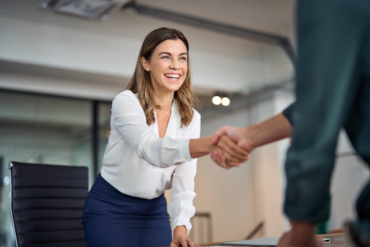 Business woman shake hand with an unidentified man on the side of a desk