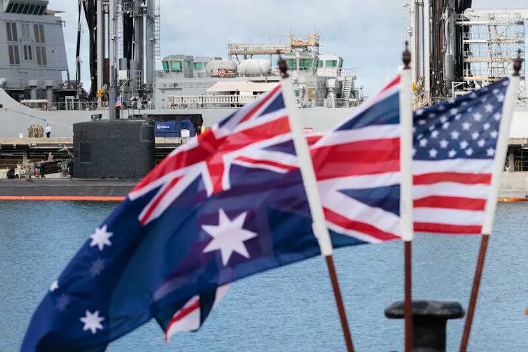 The flags of Australia, Great Britain and the USA fly next to each other in front of a navy vessel