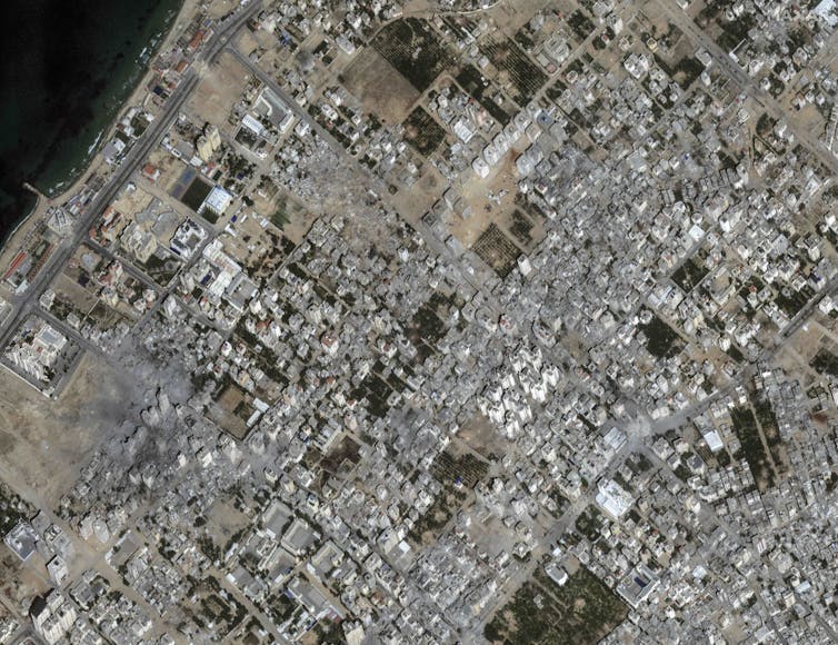 Uma foto de satélite mostrando uma área construída na qual. muitos edifícios são danificados e destruídos.