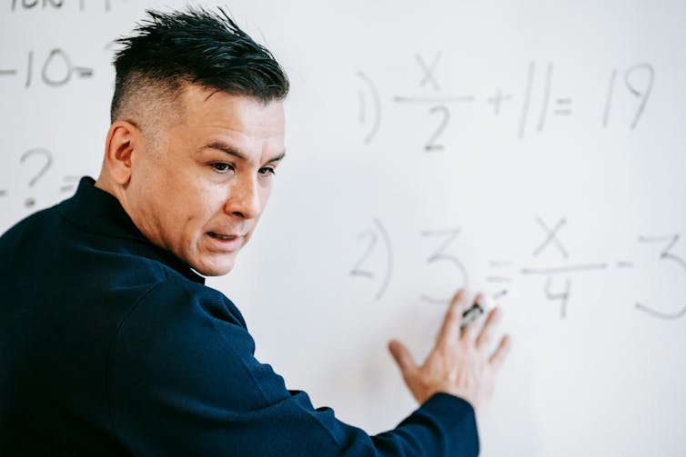 A man points to equations on a whiteboard.