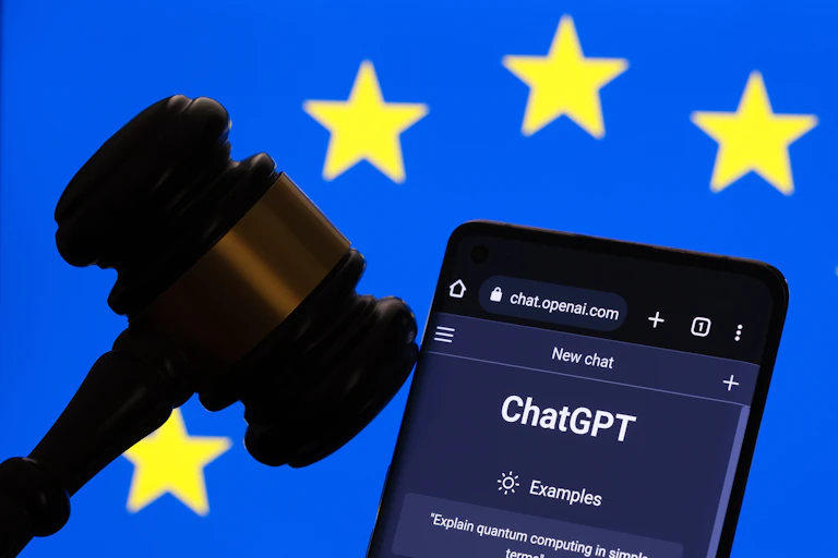Le site internet de ChatGPT ouvert sur un téléphone, à côté d'un maillet de juge, devant un drapeau européen.