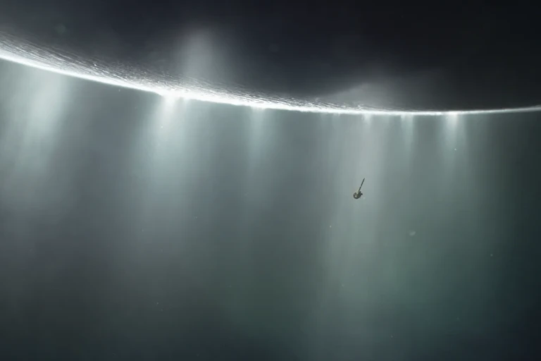 A close-up of the surface of a gray moon, with plumes of light shining off it.