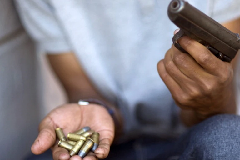 A man holds a gun in one hand and bullets in another.