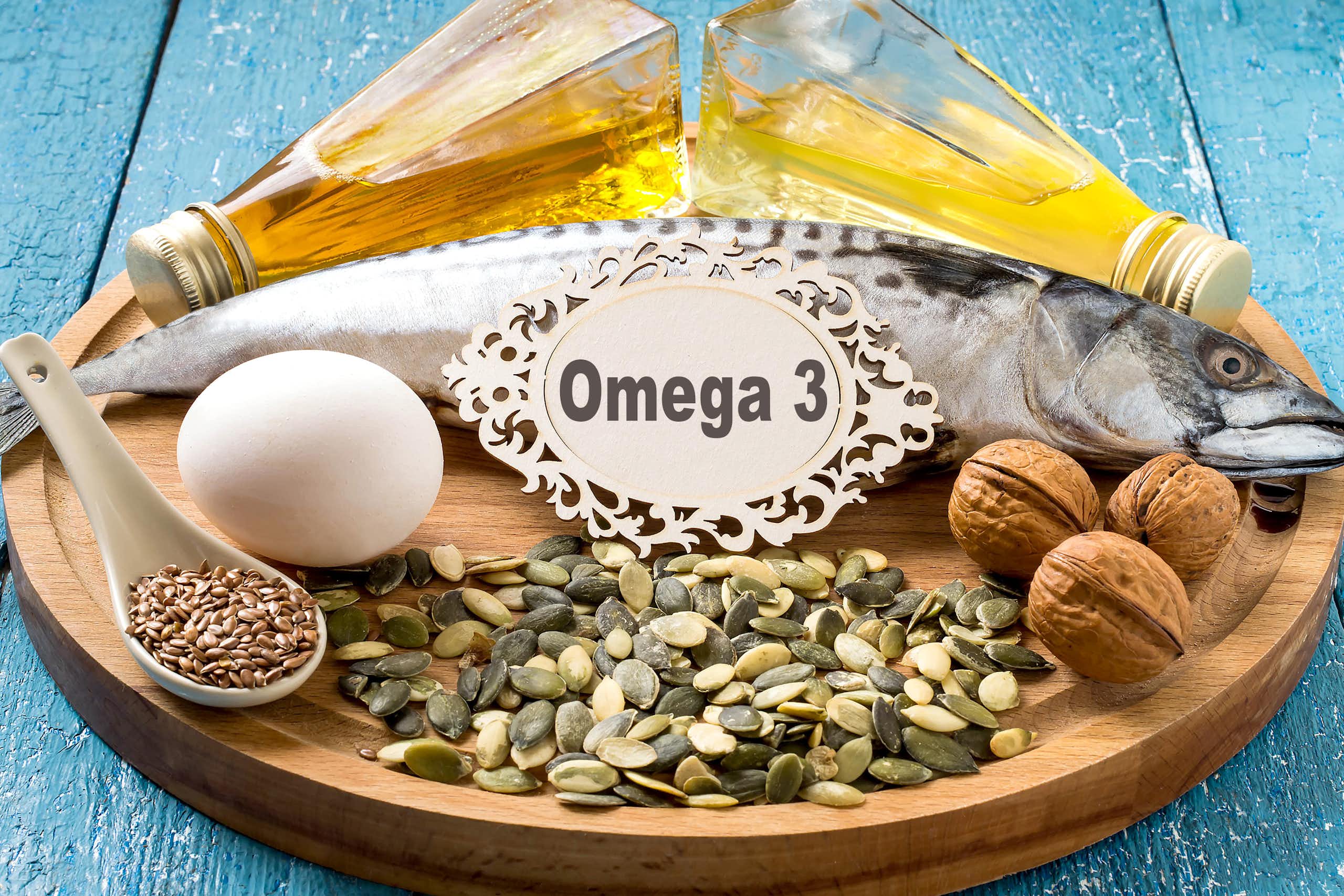 Sur un plateau, sont posé des flacons d'huile, un poisson cru, des noix, un oeuf et différentes graines. Au centre, une étiquette indique « Omega 3 »