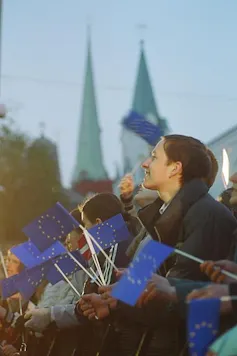 A girl smiles surrounded by people carrying blue flags with a circle of stars, the symbol of the European Union..