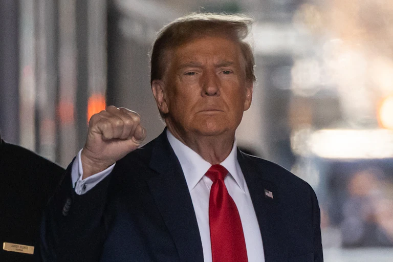 A sandy haired man in a blue suit and red tie raises a fist.