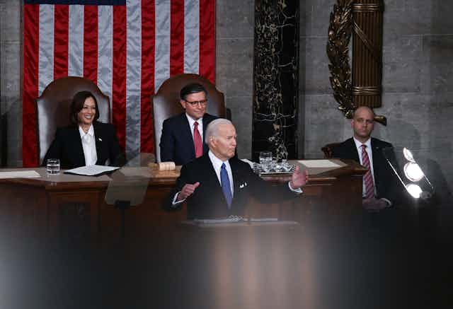 An elderly man in a suit spreads his arms as he speaks. He is flanked by a middle-aged woman and two middle-aged men.