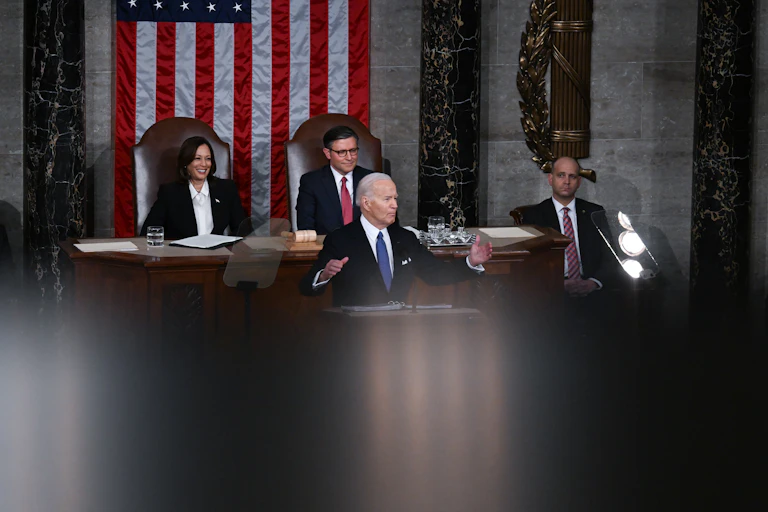 An elderly man in a suit spreads his arms as he speaks. He is flanked by a middle-aged woman and two middle-aged men.