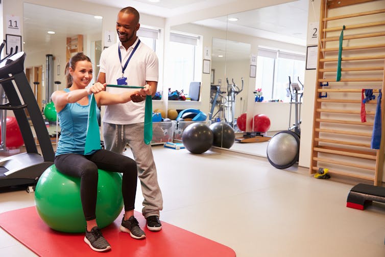 Woman sits on exercise ball and uses stretchy band