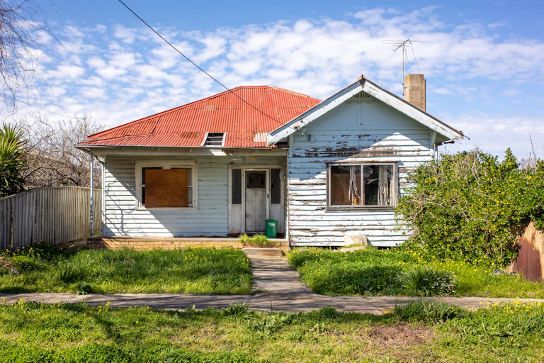 The exterior of a weatherboard house with an overgrown lawn