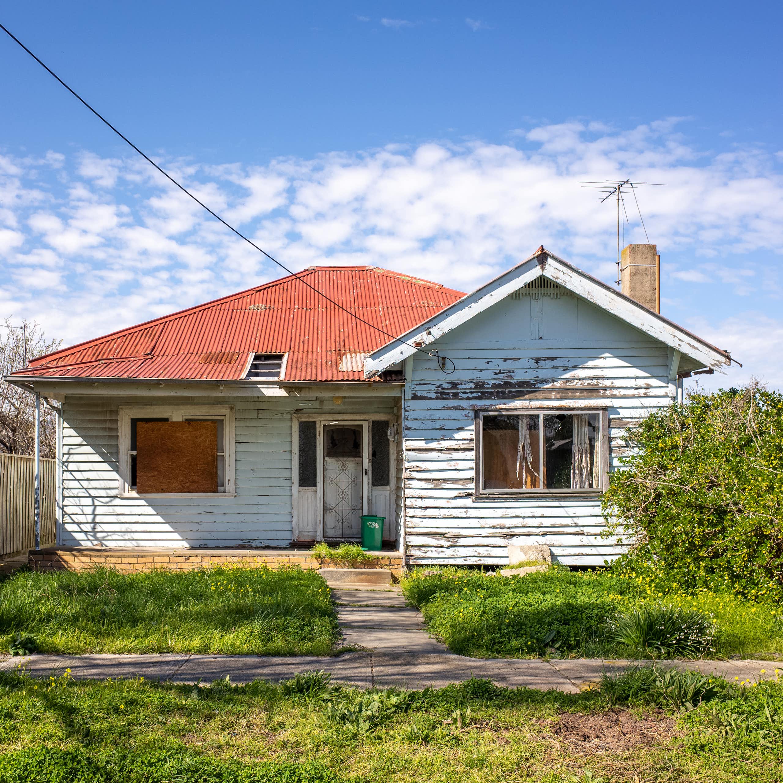The exterior of a weatherboard house with an overgrown lawn