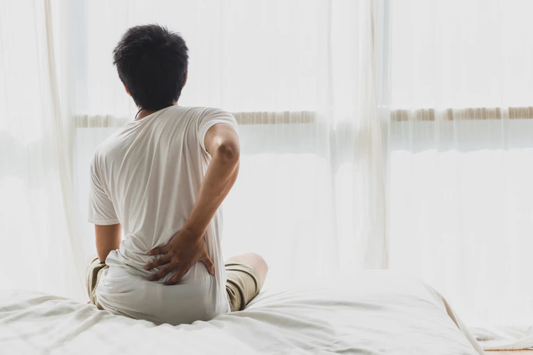 Man sits on bed in pain