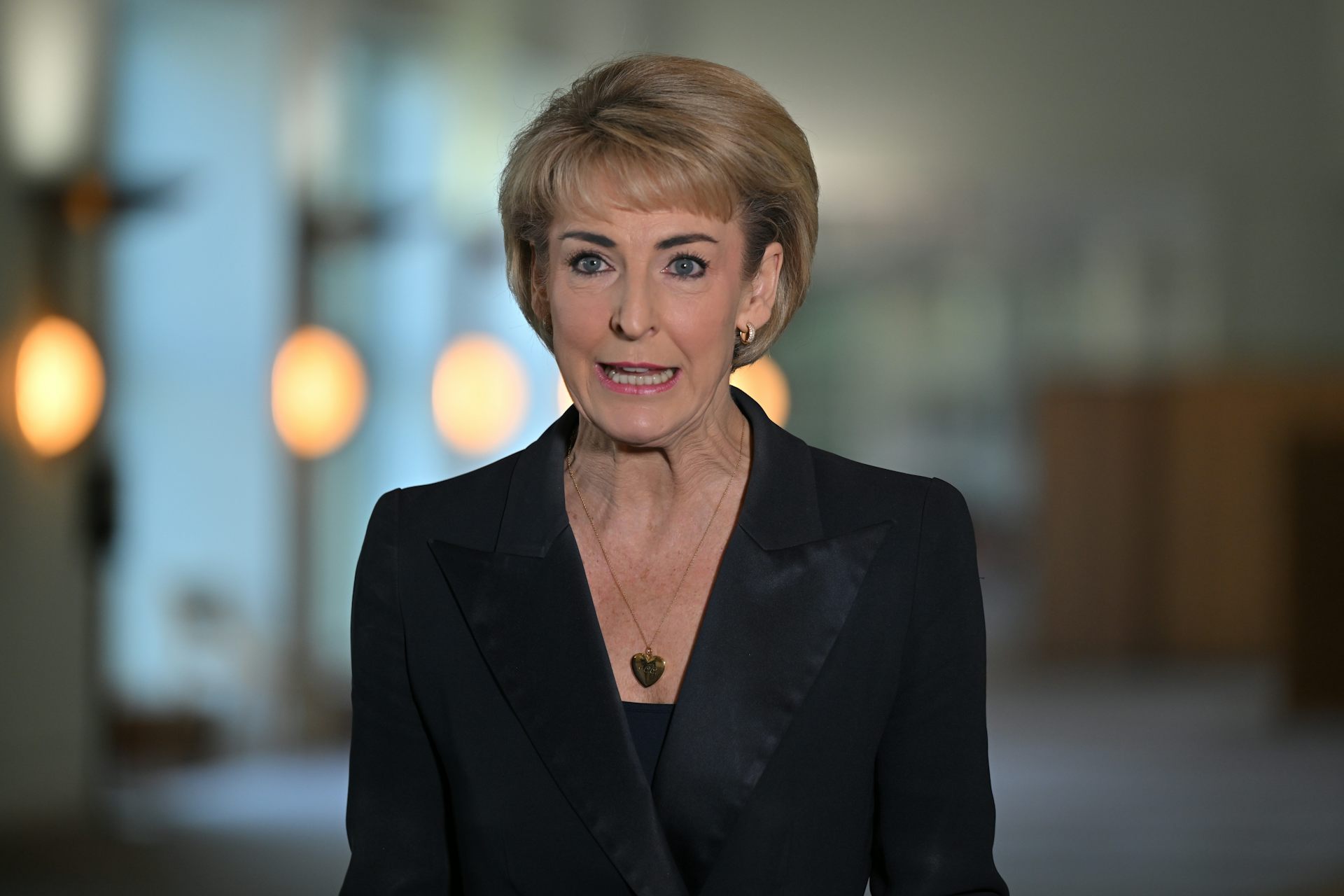 A man in a black blazer speaks at a press conference indoors