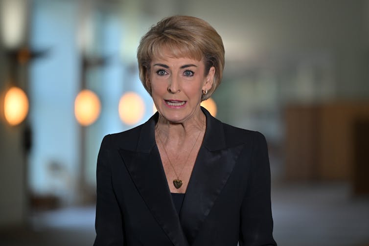 A man in a black blazer speaks at a press conference indoors