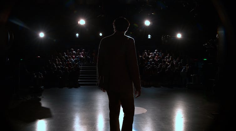 A silohouette of a man is seen as he faces towards a late-night TV show audience.