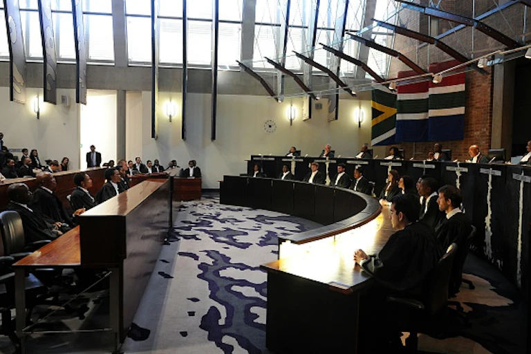 Interior of South Africa's Constitutional Court, with a row of judges and a row of clerks seated facing the courtroom.