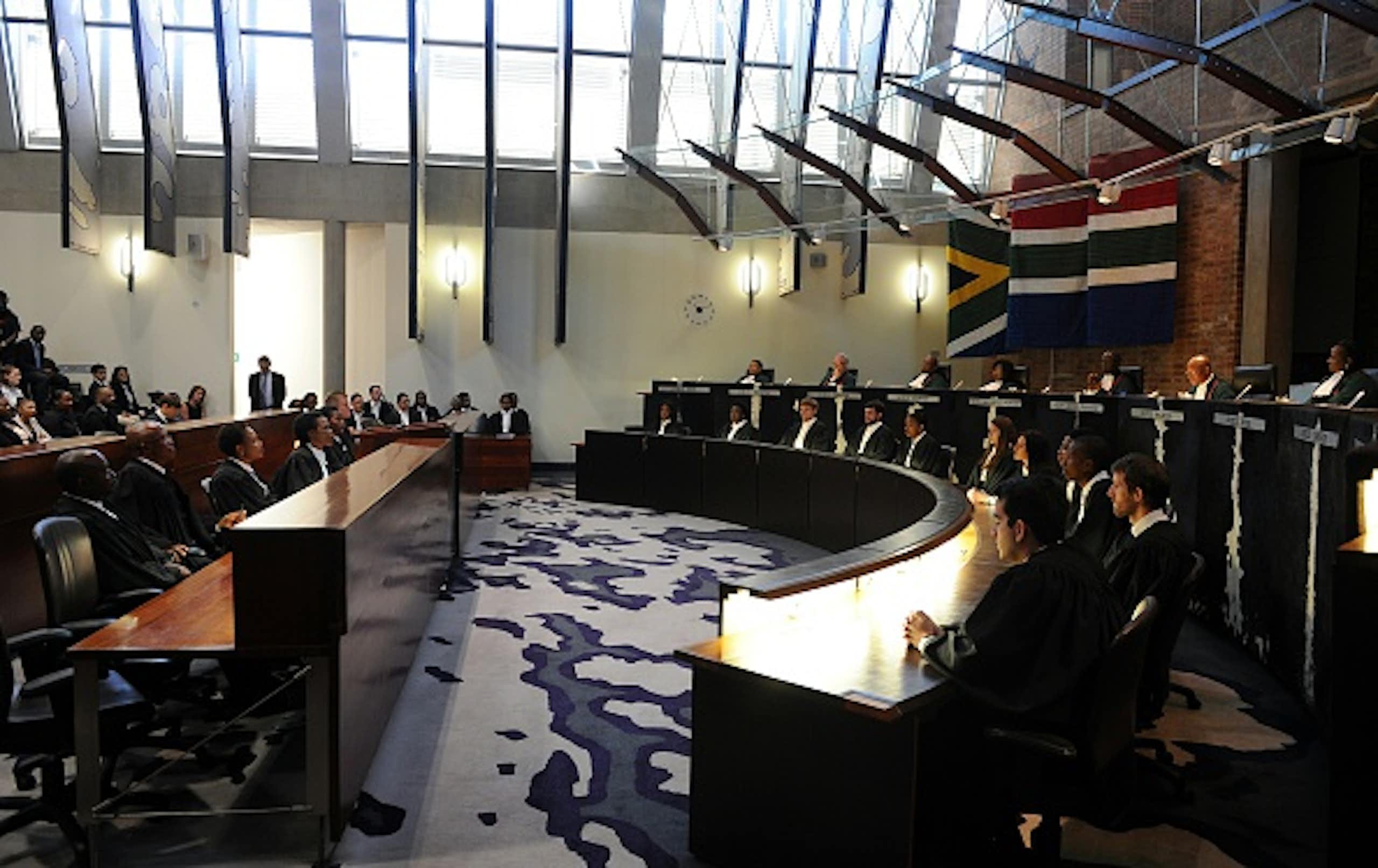Interior of South Africa's Constitutional Court, with a row of judges and a row of clerks seated facing the courtroom.