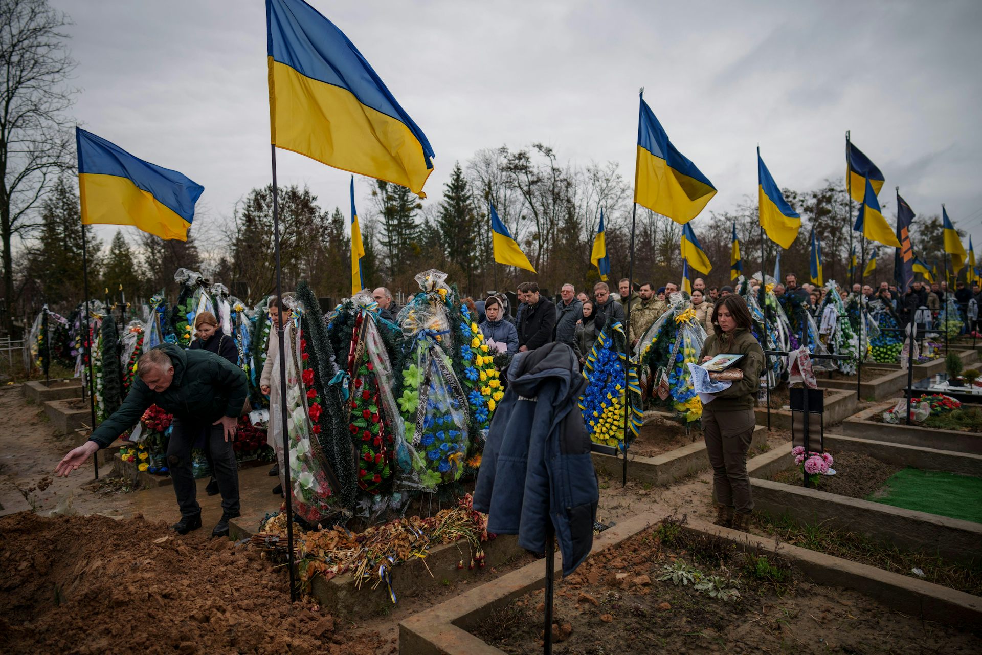 People throw dirt into the grave at the funeral of a Ukrainian soldier.