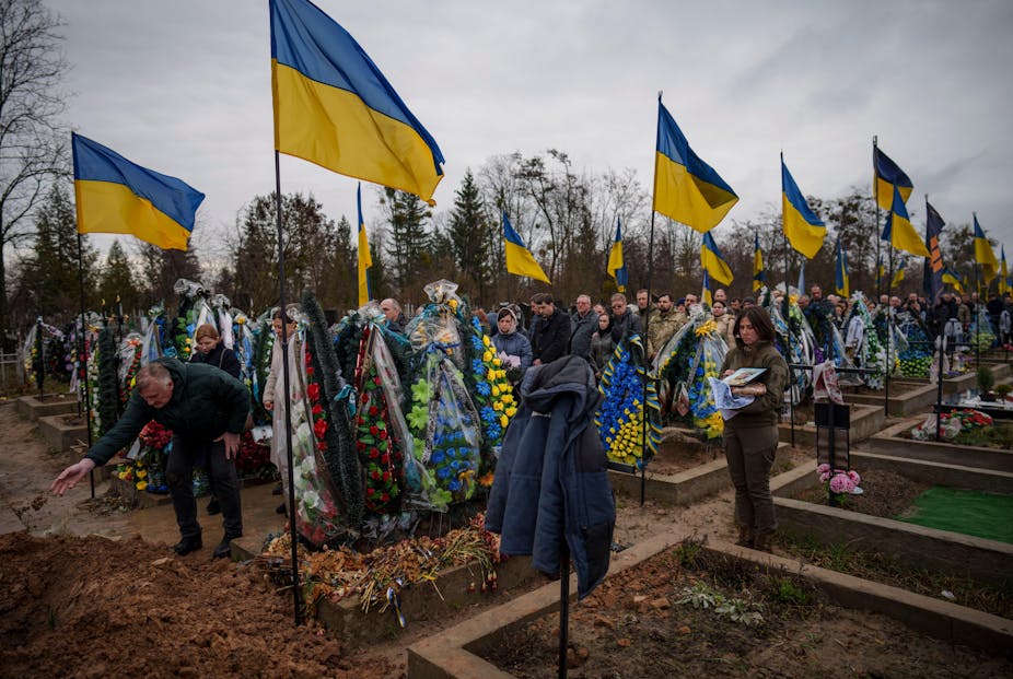 People throw dirt into the grave at the funeral of a Ukrainian soldier.