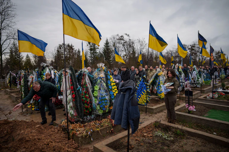People throw dirt into the grave at the funeral of a Ukrainian soldier.