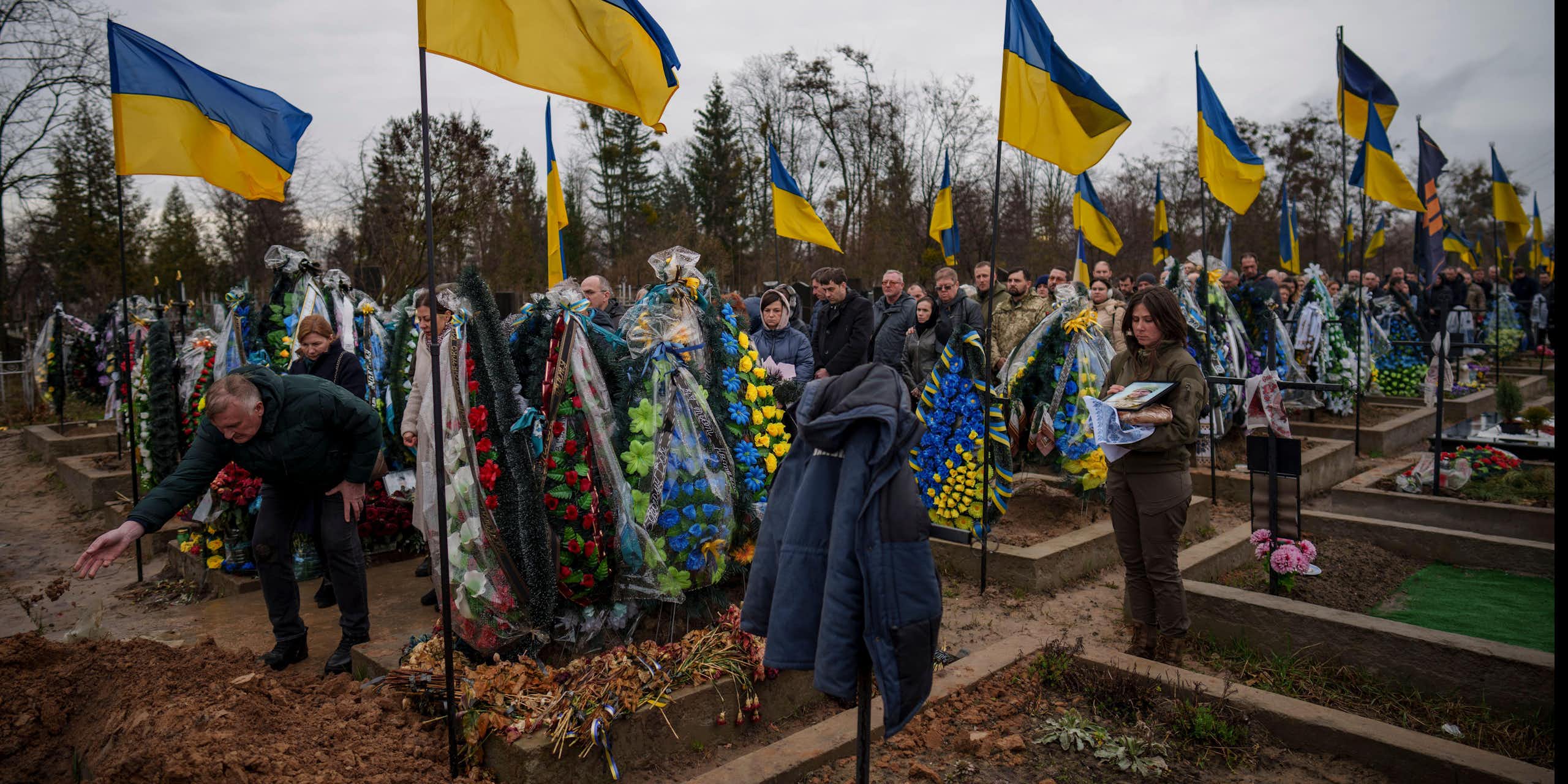 People throw dirt into the grave at the funeral of a Ukrainian soldier.